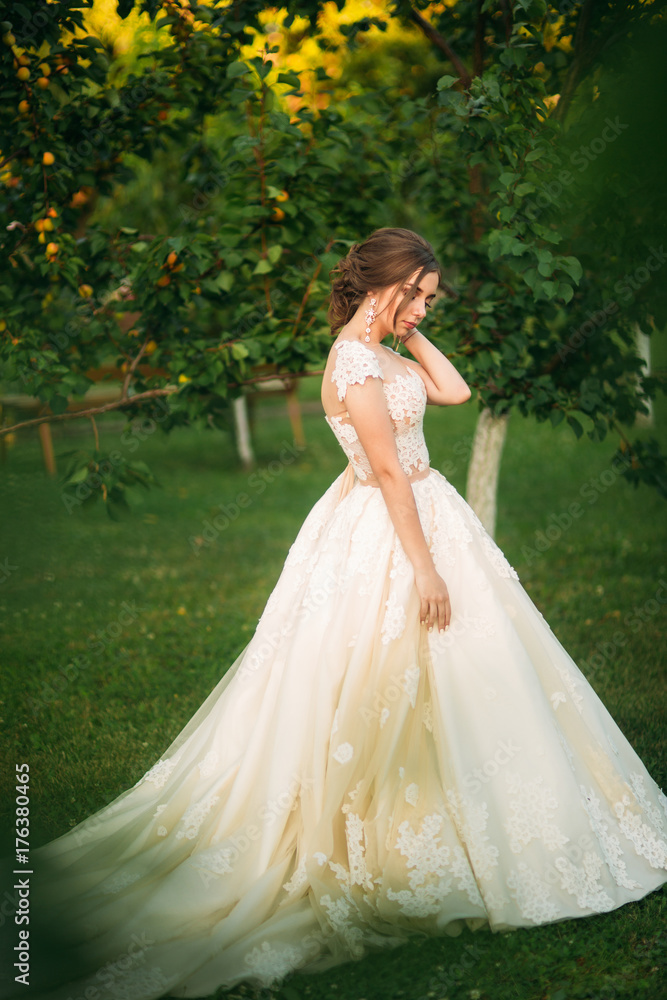 Young girl in wedding dress in park posing for photographer. Sunny weather, summer.