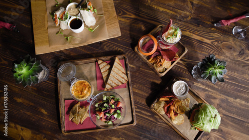 Table in the restaurant with food, view from the top. Snacks on a wooden table with a beautiful texture. Delicious sandwiches, sauces, salads and chips.