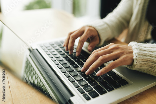 Close-up shot of unrecognizable young journalist finishing promising article with help of laptop while working from home