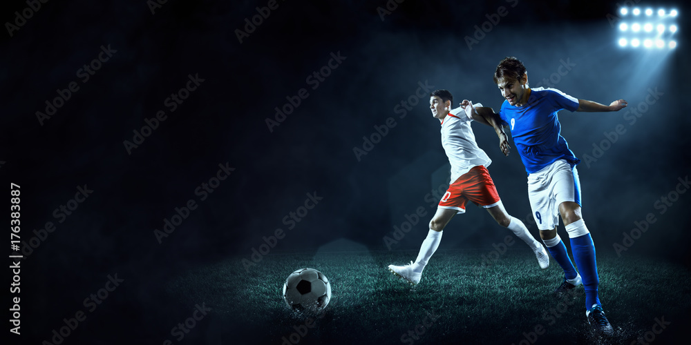 Soccer players performs an action play on a dark background. Soccer players fight for the ball. Players wears unbranded sport uniform.