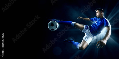 Obraz Piłkarz wykonuje akcję akcji na ciemnym tle. Gracz ma na sobie niemarkowy mundur sportowy.