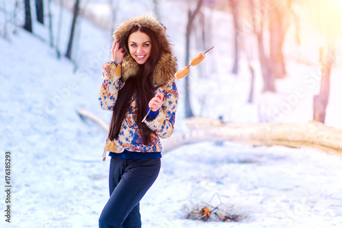 woman toasting sausages on grile in winter. woman in winter jacket near the fire photo