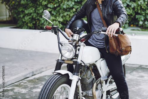 Stylish man wearing leather jacket holding helmet in hand while sitting on vintage motorcycle ready for twisted adventures