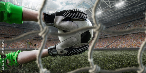 Soccer goalkeeper catches a ball on big professional football arena. View through the football goal. Goalkeeper wears unbranded sport uniform. photo