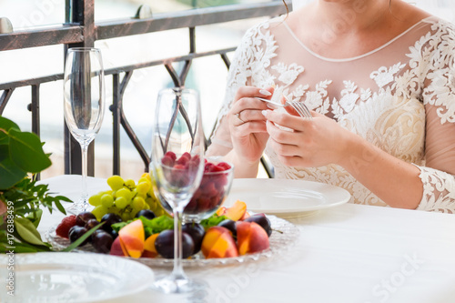 Bride and groom sitting at a table on which there is a plate of fruit.