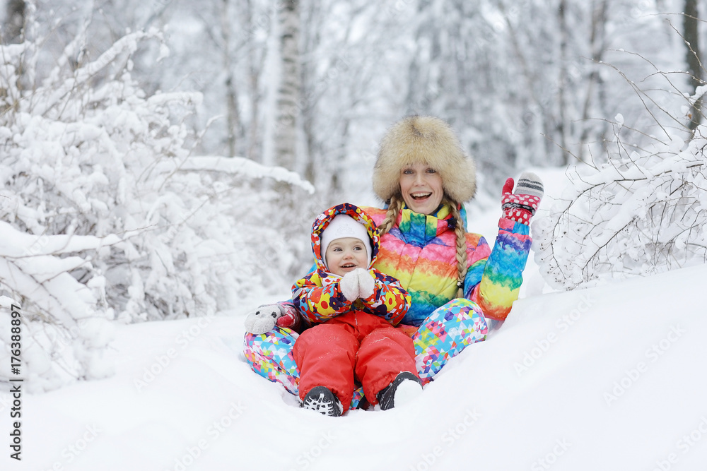 Daughter and mother are playing and lying in the snow in winter outdoors Daughter and mother are playing and lying in the snow in winter outdoors