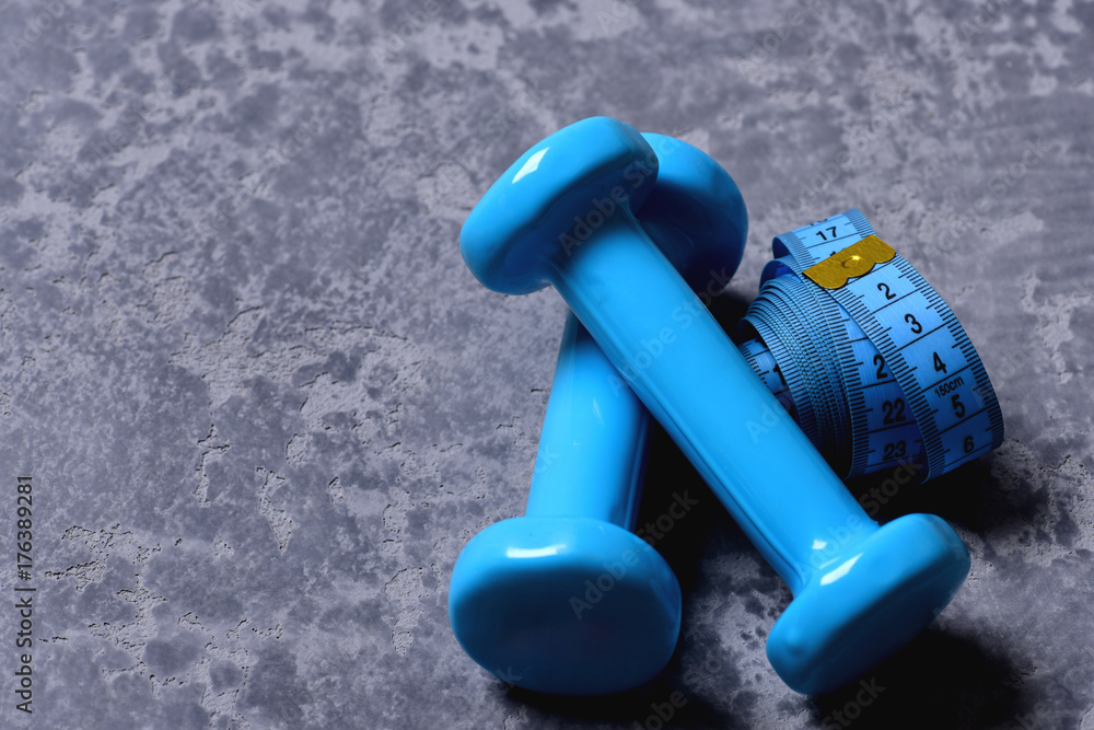 Dumbbells made of cyan blue plastic and rolled measuring tape Dumbbells made of cyan blue plastic and rolled measuring tape