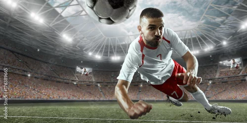Obraz Piłkarz wykonuje grę akcji i bije piłkę na profesjonalnym stadionie. Gracz ma na sobie niemarkowy mundur sportowy.