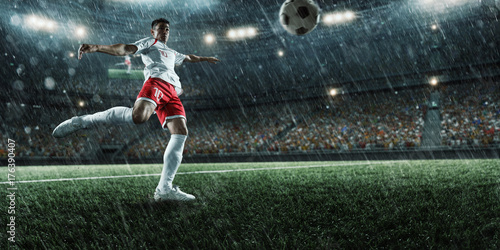 Soccer player performs an action play and beats the ball on a professional rainy stadium. Player wears unbranded sport uniform.
