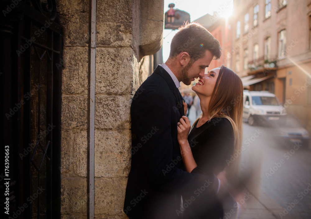 Young couple looks in each other eyes standing in the rays of sun on an old street