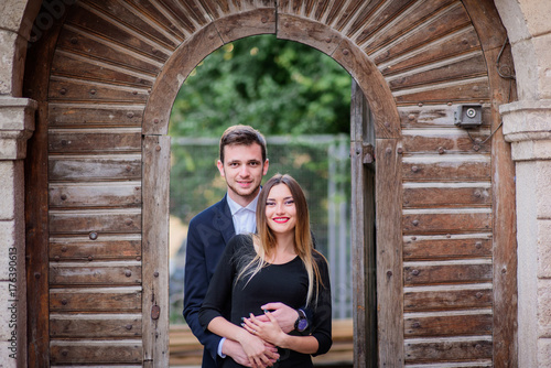 Hugging young couple stands before wooden gates