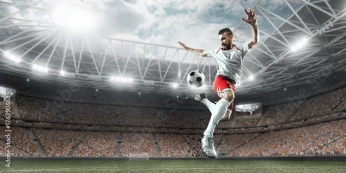Obraz Piłkarz wykonuje grę akcji i bije piłkę na profesjonalnym stadionie. Gracz ma na sobie niemarkowy mundur sportowy.