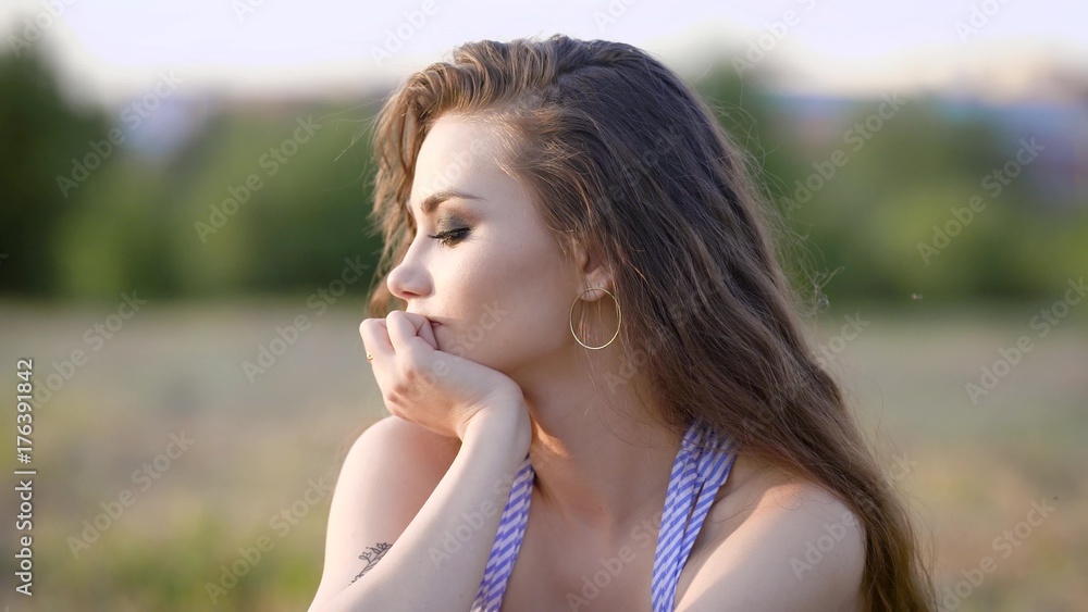 portrait of a young woman with a bright make-up and curly hair who enjoys looking out into the distance, a lady sits on nature on a warm summer day portrait of a young woman with a bright make-up and curly hair who enjoys looking out into the distance, a lady sits on nature on a warm summer day