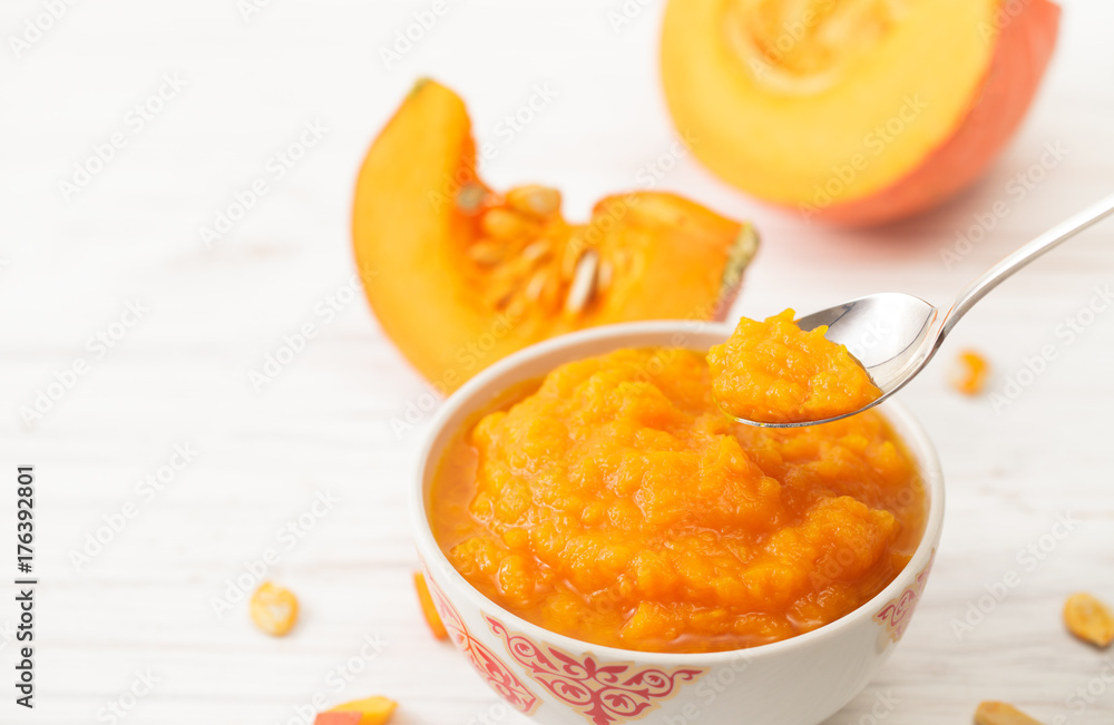 Pumpkin puree in a spoon and cut pumpkin on a white table Pumpkin puree in a spoon and cut pumpkin on a white table