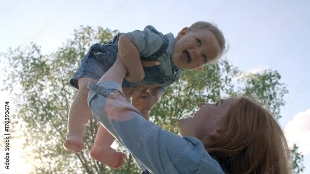 Tilt up of cheerful mother lifting laughing toddler boy in air and talking while spending time in park on sunny summer day Tilt up of cheerful mother lifting laughing toddler boy in air and talking while spending time in park on sunny summer day