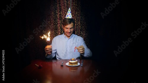 a lone man celebrates a holiday, he sits alone at a table with a cake and a candle. 4k, slow motion photo