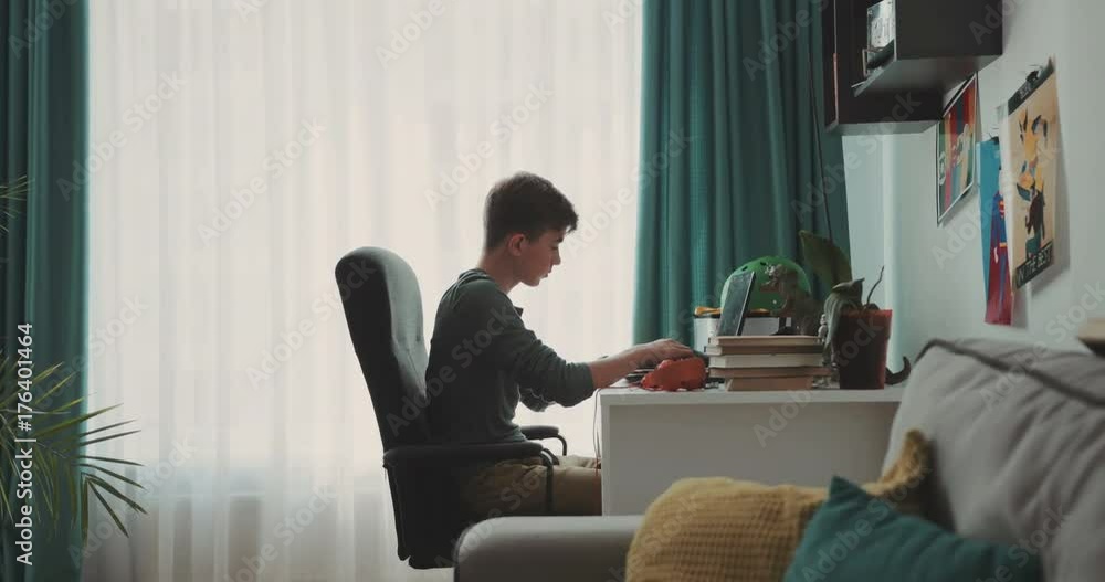 The teenager is sitting using a laptop in the home room work, homework, serious, study, school, room, bedroom. Contemporary design. Shot on RED Epic Camera. The teenager is sitting using a laptop in the home room work, homework, serious, study, school, room, bedroom. Contemporary design. Shot on RED Epic Camera.