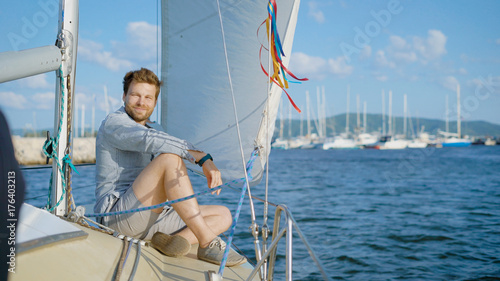 Content young man sitting on yacht and smiling at camera