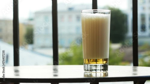 A glass of beer with high foam on the table on the balcony on a summer day photo