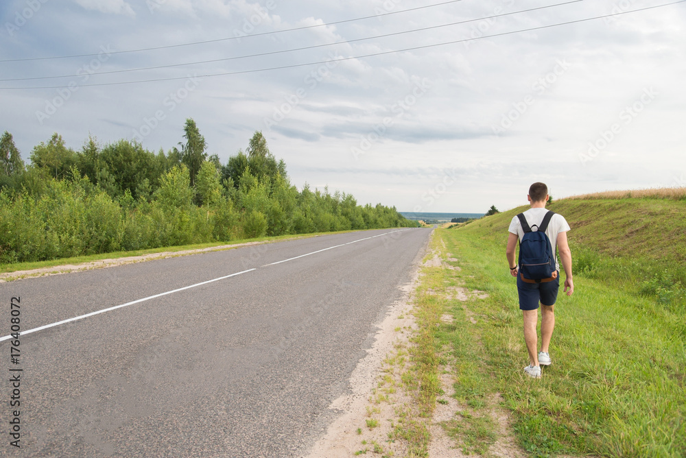 A man walking along the grass parallel to the road