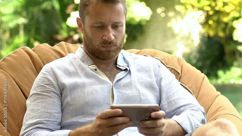 Handsome man sitting on the bean bag chair and texting messages on smartphone
Handsome man sitting on the bean bag chair and texting messages on smartphone