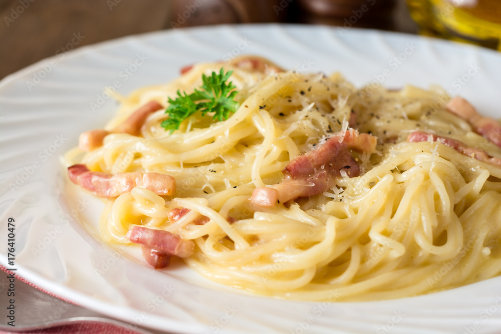 Classic pasta carbonara. Spaghetti with bacon, egg yolk and parmesan cheese on white plate on dark wooden background.