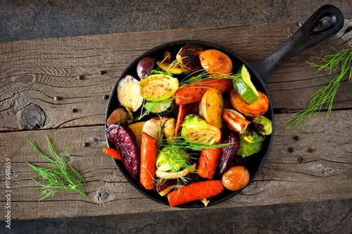 Cast iron skillet of roasted autumn vegetables against a rustic dark background photo