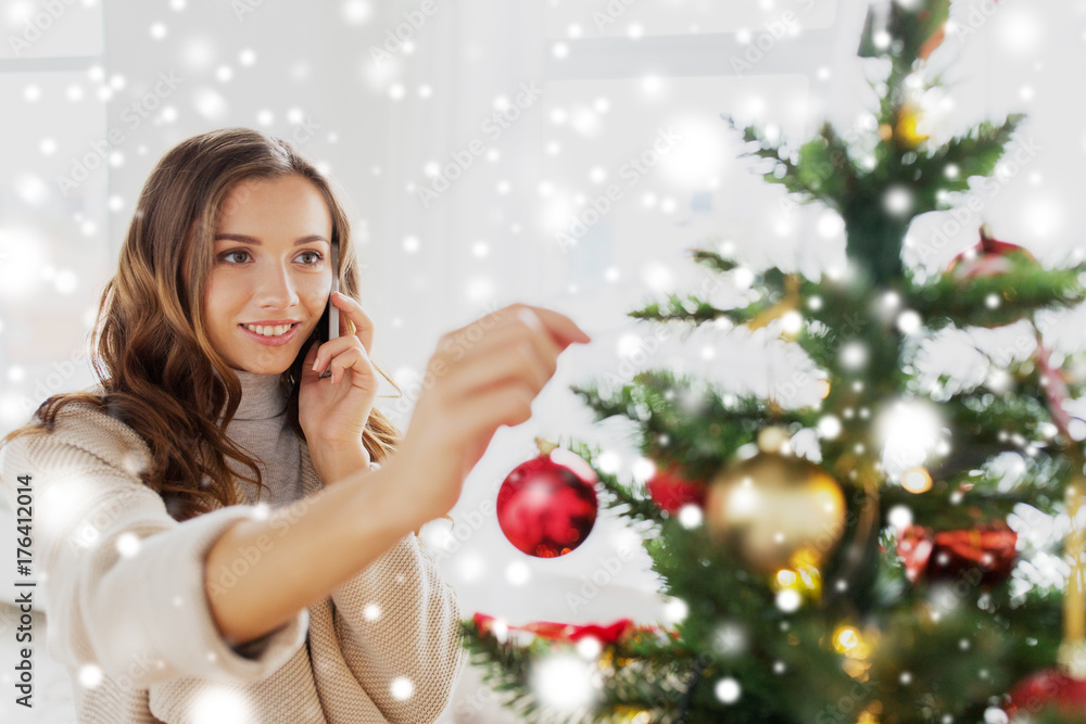 woman with smartphone decorating christmas tree