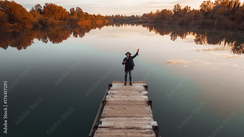 Giovane ragazzo che sta seduto su un molo di un lago 