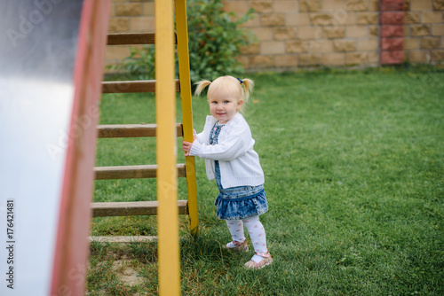 portrait of beautiful blonde little child girl with big blue eyes and a sweet smile playing outdoors on background of green grass