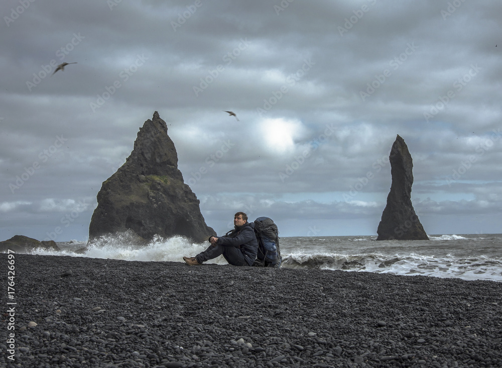 Tourist with backpack seatting on the Black sand beach, Vik in Iceland
