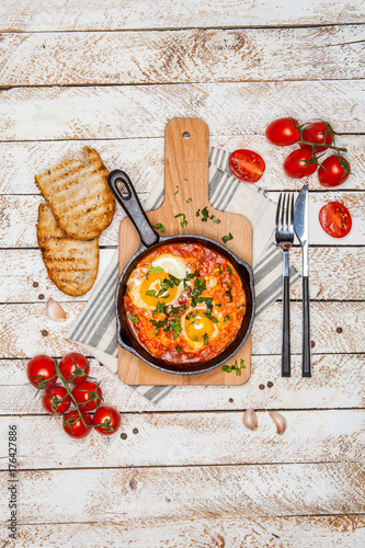 Breakfast. Shakshuka with bread in pan on a black rustic background. Fried eggs with tomatoes. Top view. Space for text. Middle eastern style breakfast or lunch