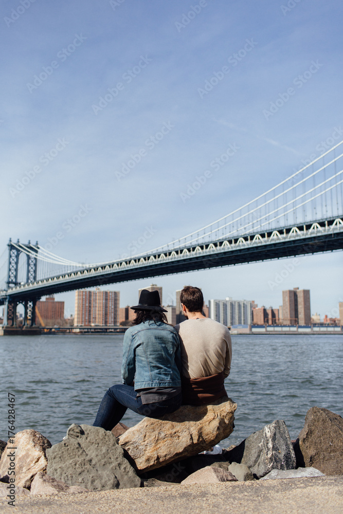 Young couple sitting on the rock along the East River, Brooklyn Young couple sitting on the rock along the East River, Brooklyn