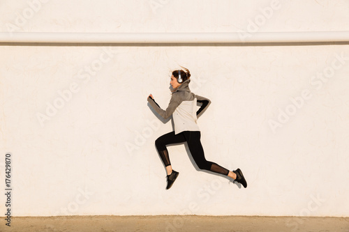 Full length photo of young fitness woman in sport wear jumping near white wall