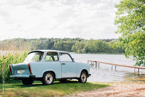 Fotografie Blue GDR Vintage Car Parked Near Lake on Sunny Summer Day