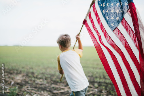 boy running through a field, holding an American flag photo