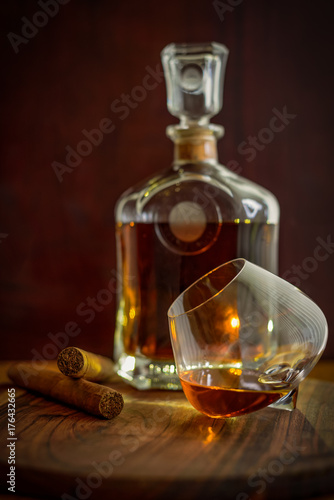 Two cigars, a glass and a bottle of rum on a wooden surface