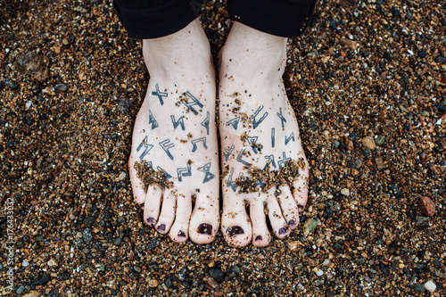 Transgender persons feet with painted nails and runes tattoos