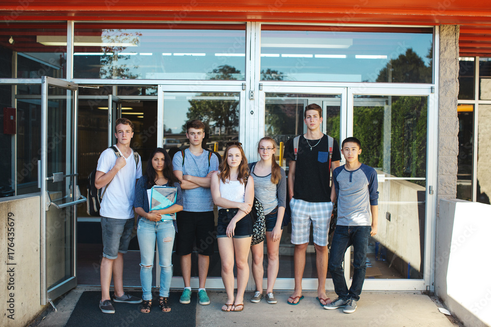 Group of serious high school teens standing in front of school on summer day Group of serious high school teens standing in front of school on summer day