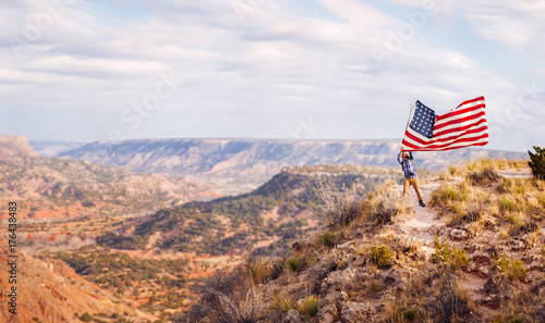 Man waving an American flag while standing on canyon photo