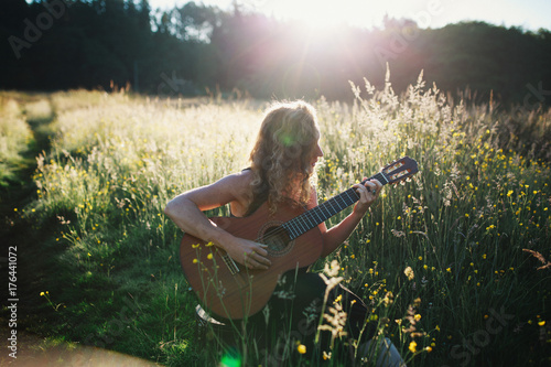 Young woman sitting in field at sunrise playing classical guitar and singing photo