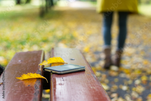 Forgotten smartphone on a park bench. Woman is leaving from a bench where she lost her cell phone.  photo