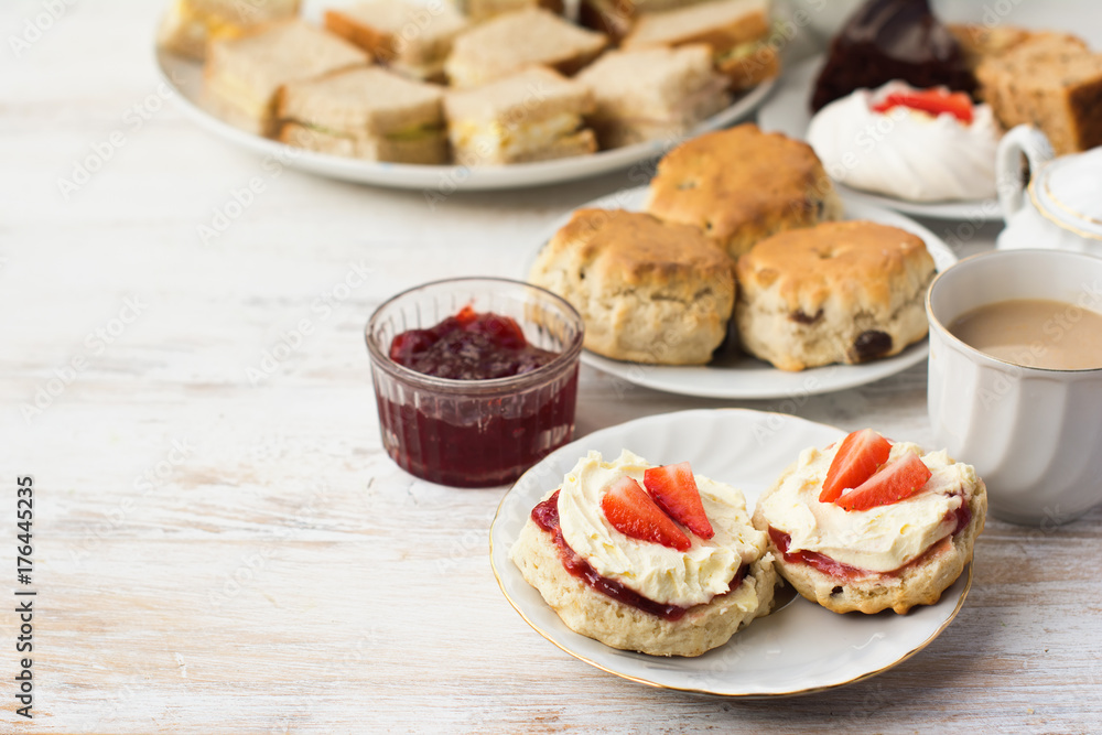 English cream teas, scones with jam and cream, tea with milk, with sandwiches on the back, on the white wooden table, selective focus copy space for text