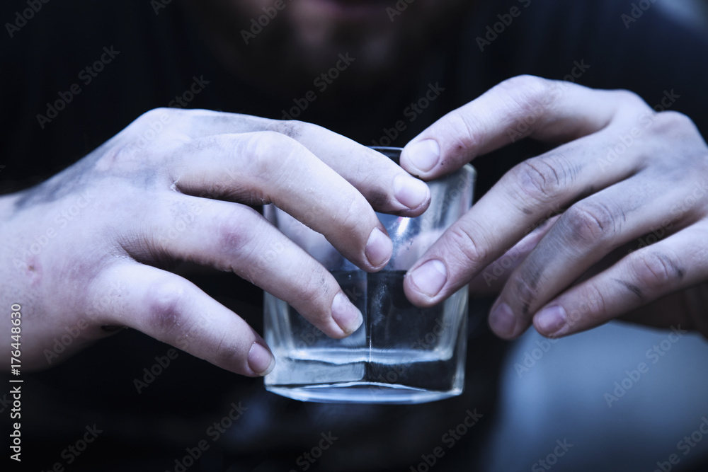 Close up of dirty man holding a glass of vodka. Drunk young people. (alcoholism, pain, pity, hopelessness, social problem of dependence concept)