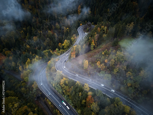 street from above trough a misty forest at autumn, aerial view flying through the clouds with fog and trees