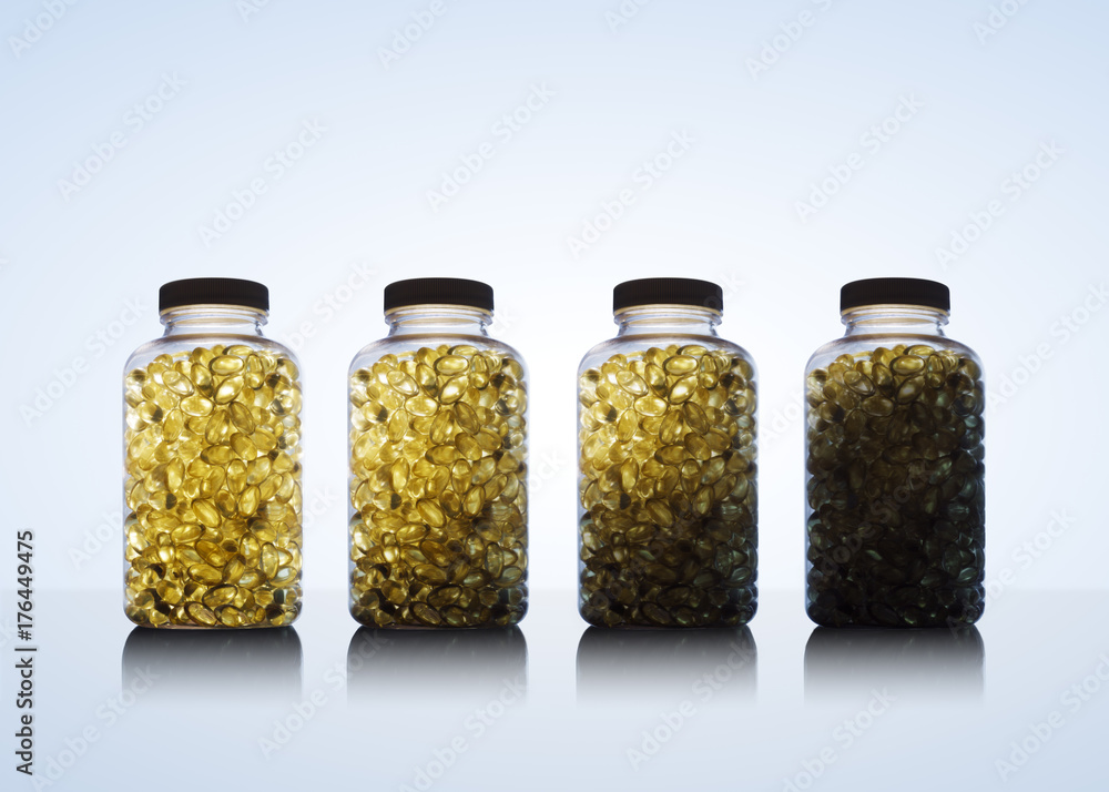 Amber glow through bottles full of fish oil omega 3 and vitamin D supplement gel capsules. on blue background Amber glow through bottles full of fish oil omega 3 and vitamin D supplement gel capsules. on blue background