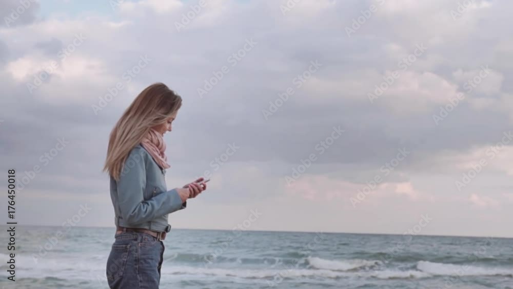 Young beautiful girl is looking at the phone on the ocean shore. The camera panarizes a close-up Young beautiful girl is looking at the phone on the ocean shore. The camera panarizes a close-up
