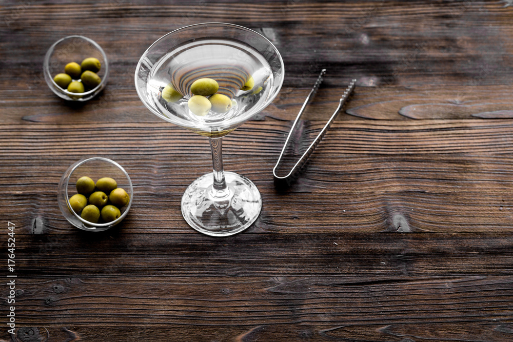 Make martini cocktails. Glass with beverage, olives and utensils on dark wooden background top view copyspace Make martini cocktails. Glass with beverage, olives and utensils on dark wooden background top view copyspace