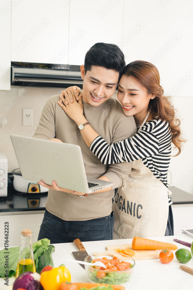Asian woman showing something on the laptop to her boyfriend in the kitchen Asian woman showing something on the laptop to her boyfriend in the kitchen