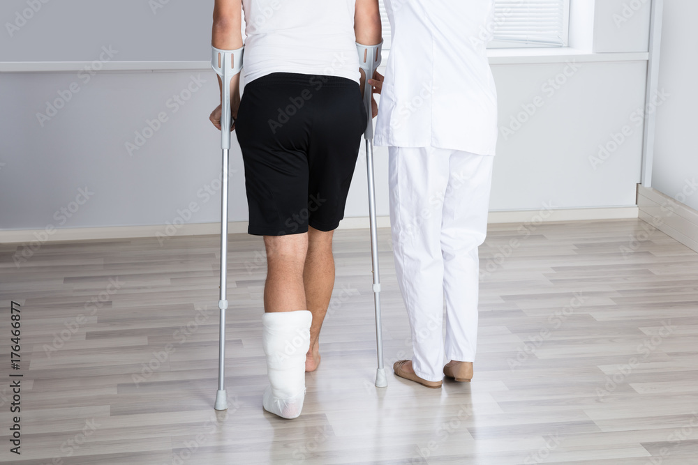 Physiotherapist Helping Injured Man To Walk With Crutches Physiotherapist Helping Injured Man To Walk With Crutches